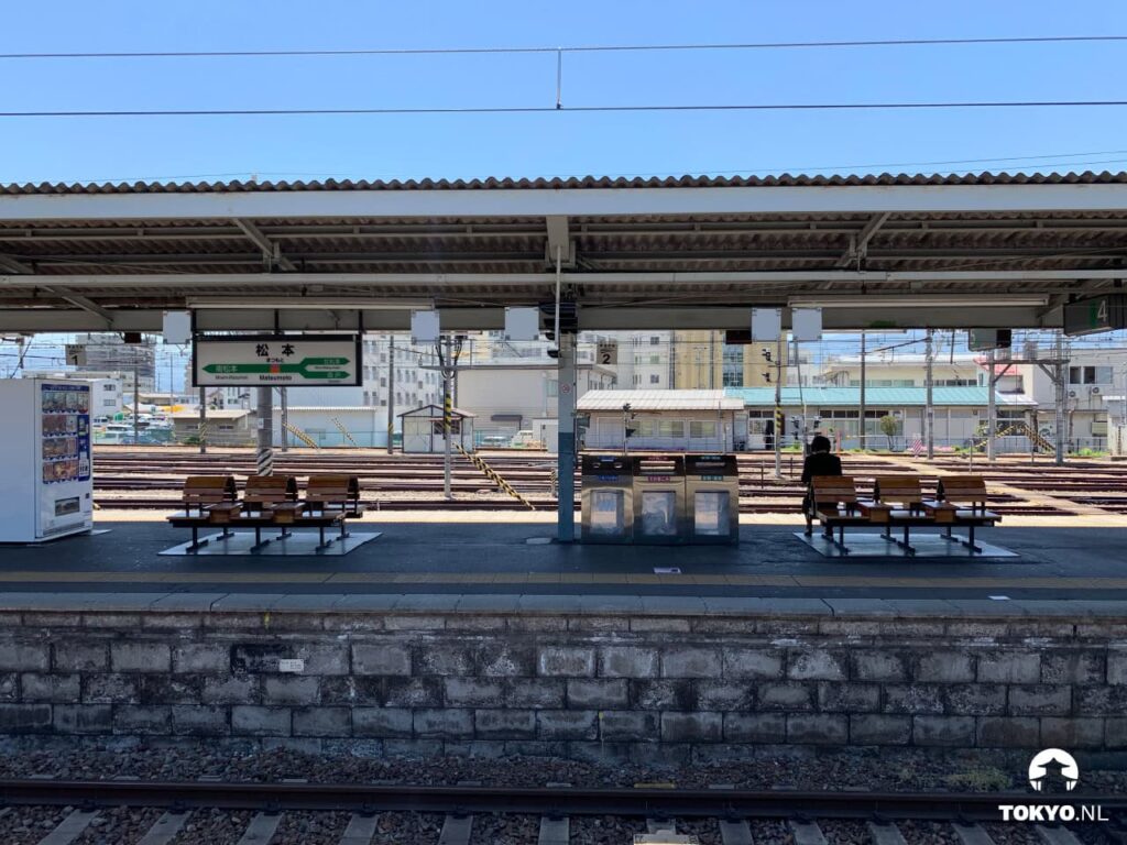 Leerer Bahnsteig des Bahnhofs Matsumoto mit Blick auf Gleise und Züge an einem sonnigen Tag