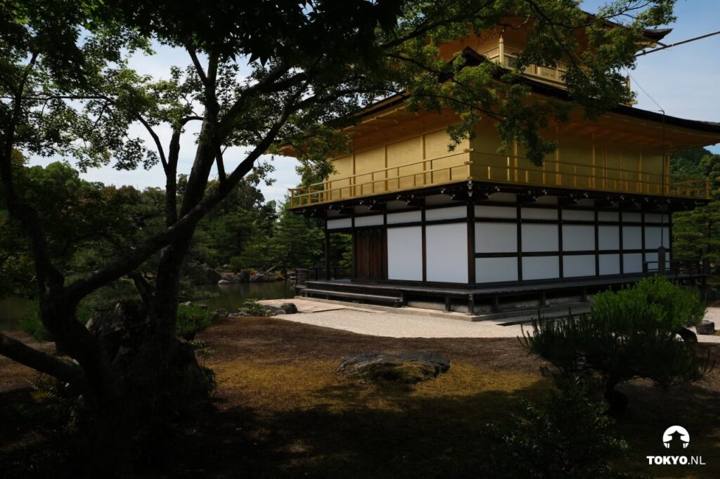The Golden Pavilion viewed from a different angle, showing its distinctive architecture with gold-leafed upper floors and traditional Japanese roof design, set within a meticulously maintained garden.
