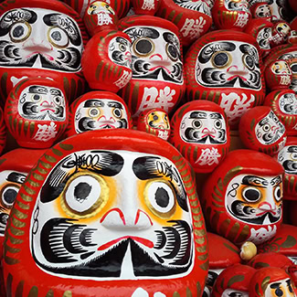 Mehrere Daruma-Puppen mit roten Gesichtern als japanische Glücksbringer, dicht nebeneinander aufgestapelt