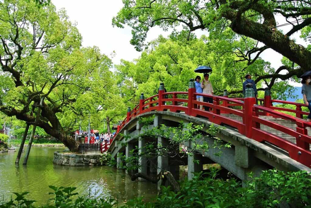 Rote Holzbrücke über Teich in japanischem Garten mit grünen Bäumen