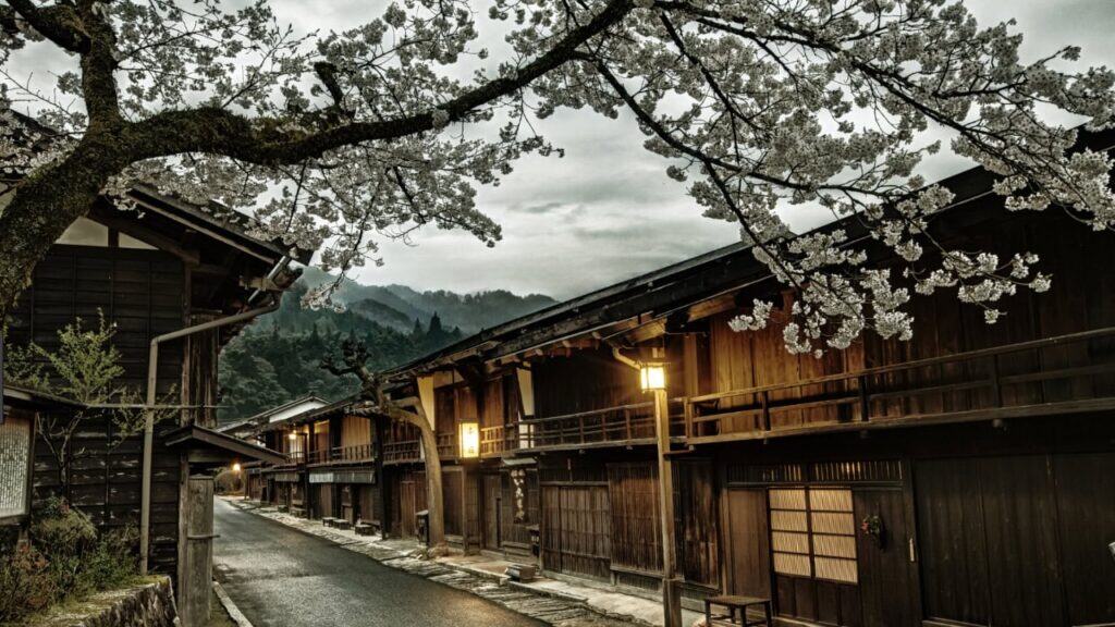 Traditionelle japanische Holzhäuser mit charakteristischen Dächern unter blühenden Kirschbäumen in einem historischen Dorf