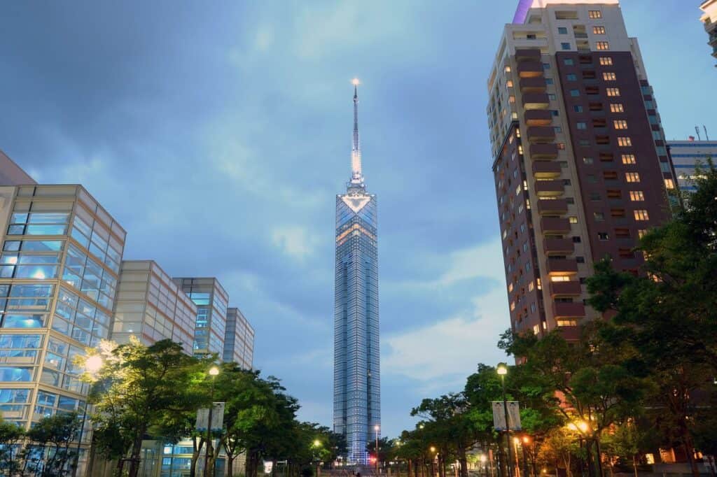 Beleuchteter Fukuoka Tower zwischen modernen Gebäuden in der Abenddämmerung