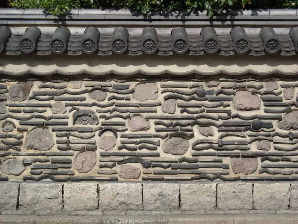 Traditionelle japanische Mauer mit kunstvollem Steinmuster und Dachziegeln