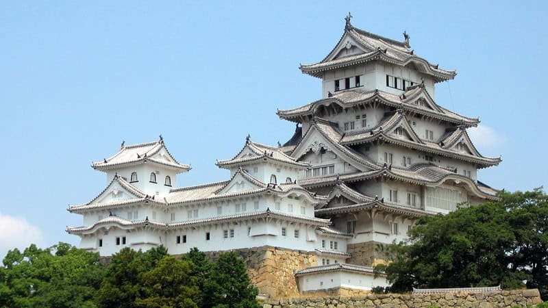 Das weiße "Reiher-Schloss" Himeji vor blauem Himmel und grünen Bäumen