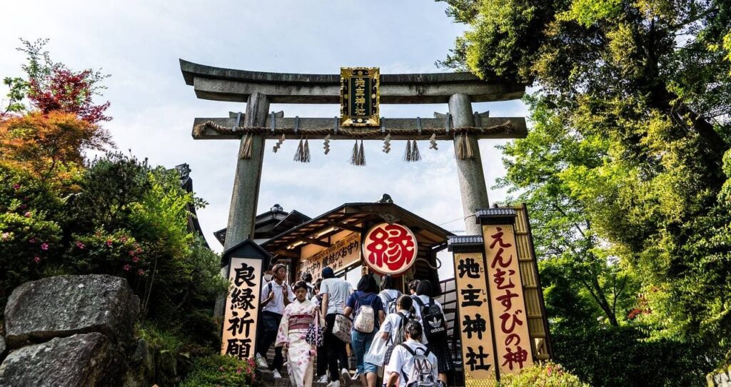 Traditionelles Torii-Tor am Jishu-Schrein innerhalb des Kiyomizu-dera Komplexes mit Besuchern in Kimono und japanischen Schriftzeichen