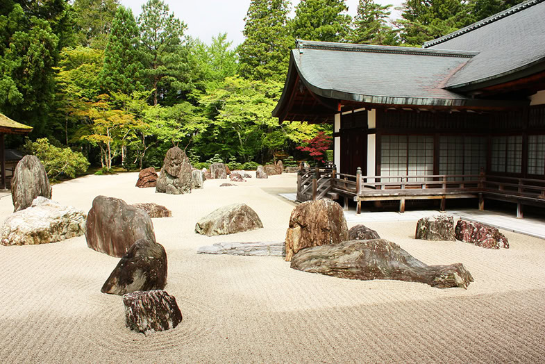 Der Garten des Tempels mit Steinen und Sand neben dem Gebäude und grünen Bäumen im Hintergrund