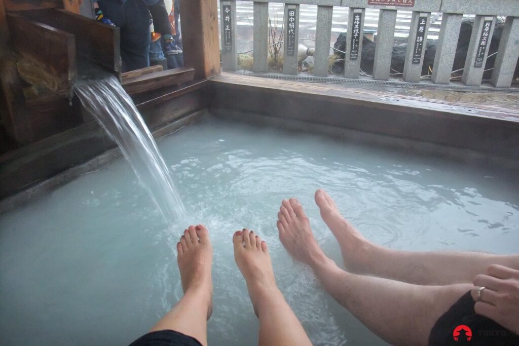 Japanisches Onsen-Fußbad mit zwei Personen beim entspannten Baden, klarem Mineralwasser und Wasserfontäne für Wellness-Erlebnis