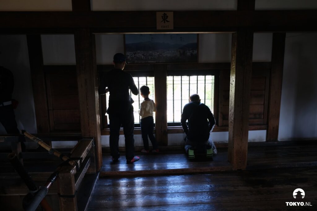 Besucher im Inneren des Matsumoto-Schlosses mit Blick nach Osten durch ein Gitterfenster