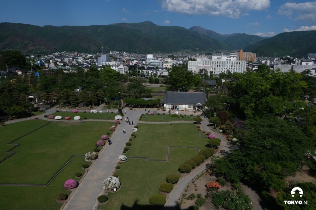 Blick auf den Schlossgarten von Matsumoto und die Stadt mit umgebenden Bergen an einem klaren Tag