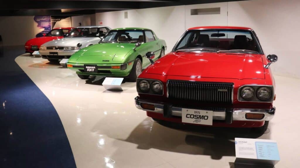 Vintage Mazda-Fahrzeuge im Mazda Museum Hiroshima, darunter ein roter Cosmo und grüne RX-7 Sportwagen