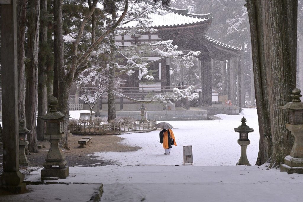 Mönch im Mittelpunkt von einer Baumallee im Schnee und im Hintergrund ein japanischer Tempel
