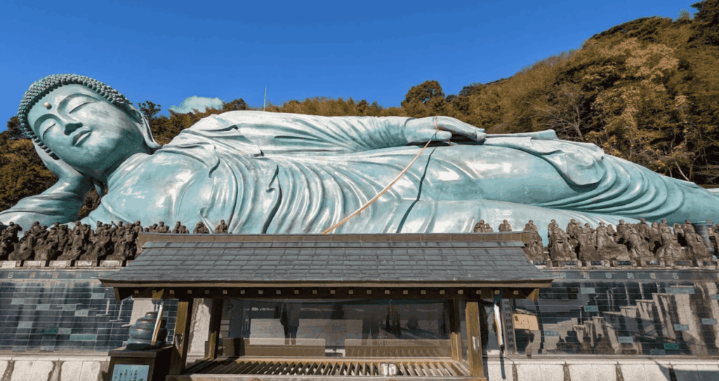 Riesige liegende Buddha-Statue aus Bronze vor bewaldeten Hügeln