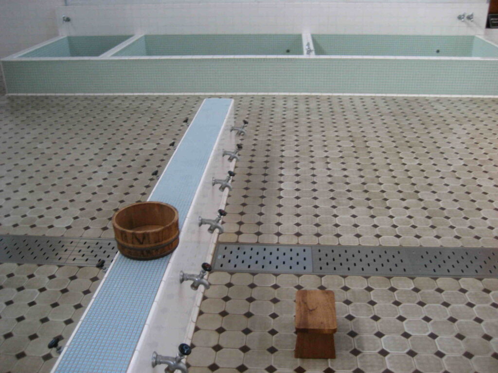 Traditioneller japanischer Onsen-Waschbereich mit grünen Mineralwasserbecken, Mosaikfliesen und authentischen Holzeimern zum Körperreinigen