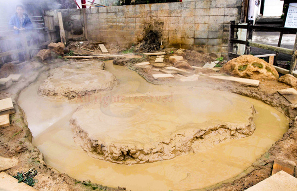 Geothermales Onsen-Becken mit trübem Mineralwasser, natürlichen Sedimenten und traditioneller japanischer Holzarchitektur für authentisches Badeerlebnis