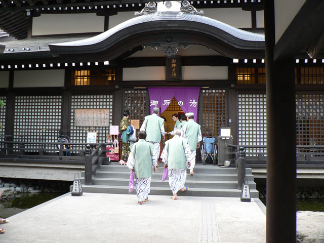 Japanische Yukata-Träger in traditioneller Kleidung vor historischem Onsen-Tempel mit klassischer Holzarchitektur und spiritueller Atmosphäre