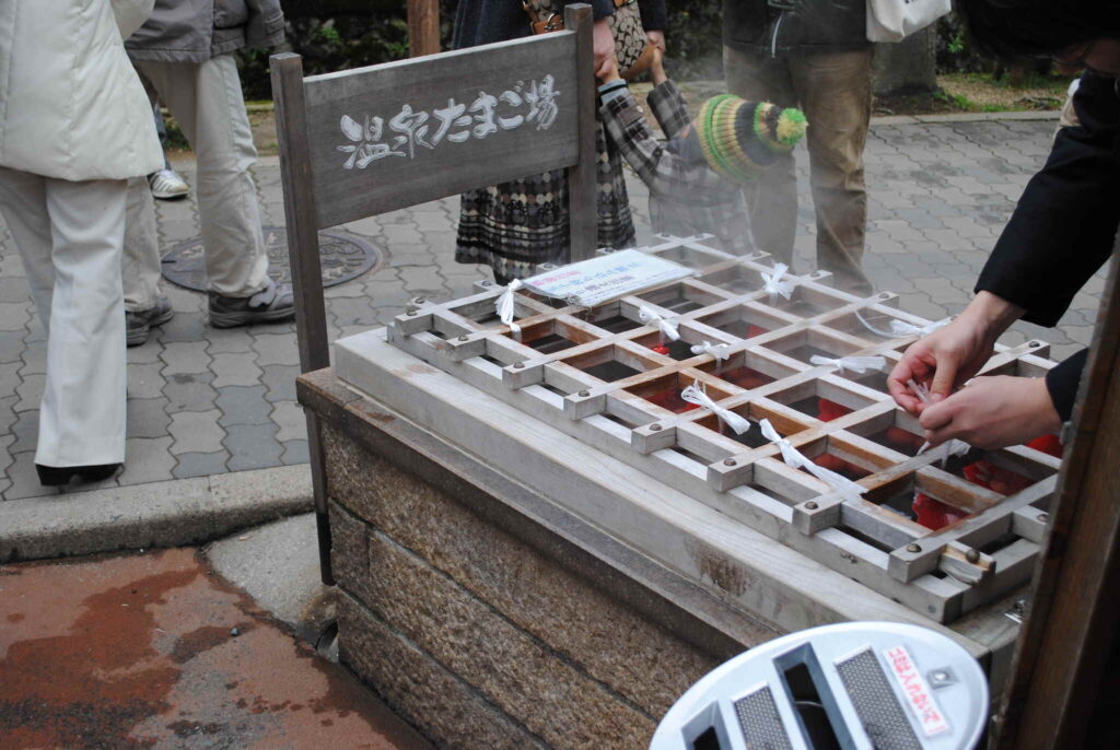 Traditioneller japanischer Onsen-Temperaturtest mit Holzgitter über heißem Quellwasser und Besuchern beim Prüfen der Wassertemperatur