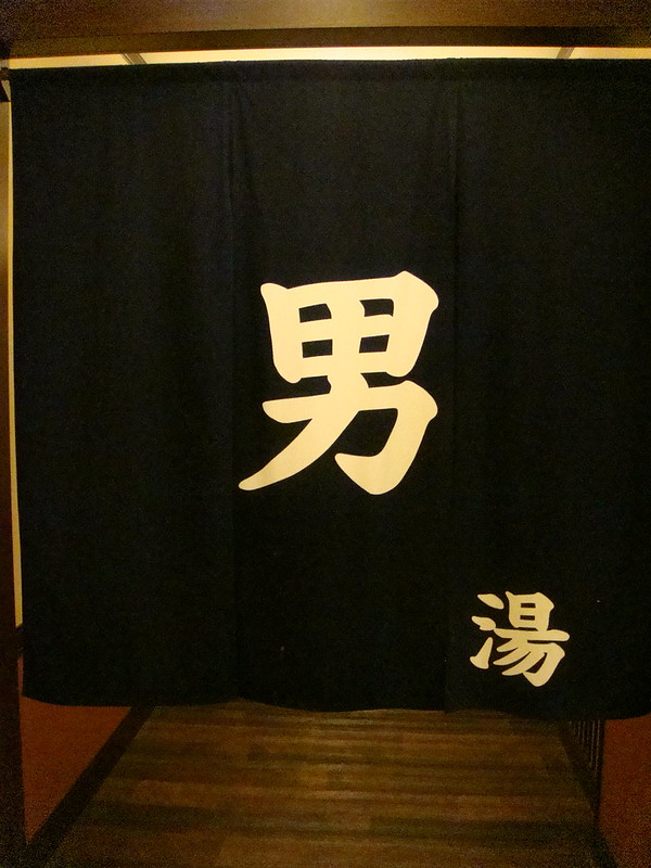 Schwarze Noren-Vorhänge mit japanischen Schriftzeichen "男湯" (Herrenbad) am Eingang eines traditionellen Onsen-Badehauses