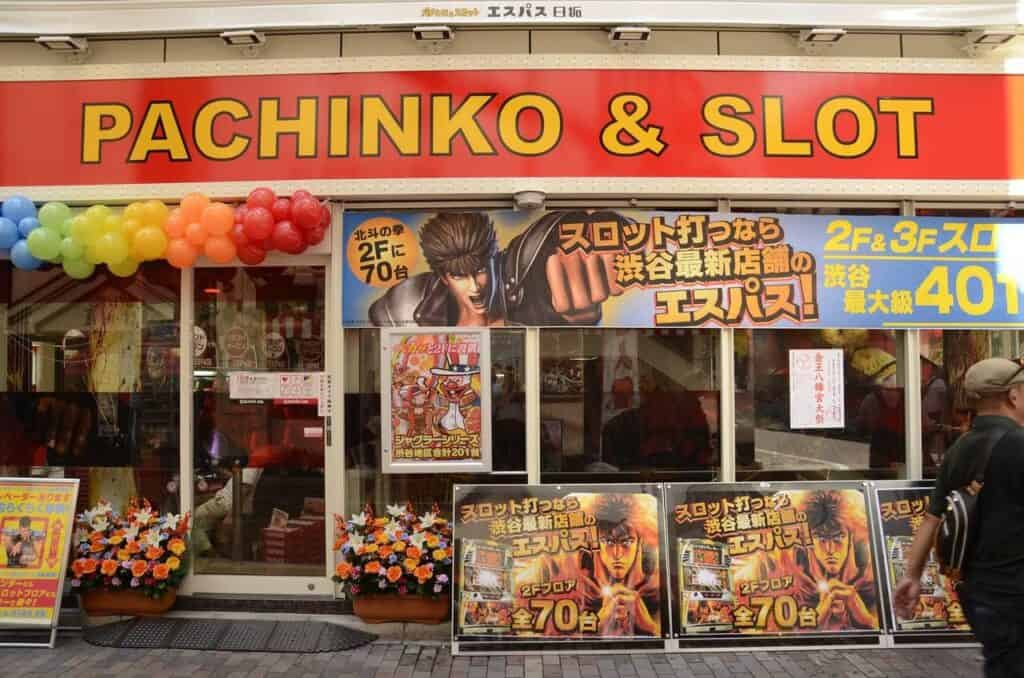 Außenansicht einer Pachinko & Slot-Halle mit bunten Anime-Werbeplakaten und charakteristischer japanischer Spielhallen-Fassade