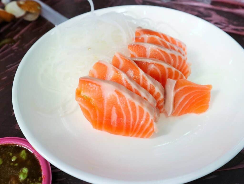 Frisches Lachs-Sashimi in dünnen Scheiben auf weißem Teller, perfekt geschnitten mit sichtbarer Marmorierung