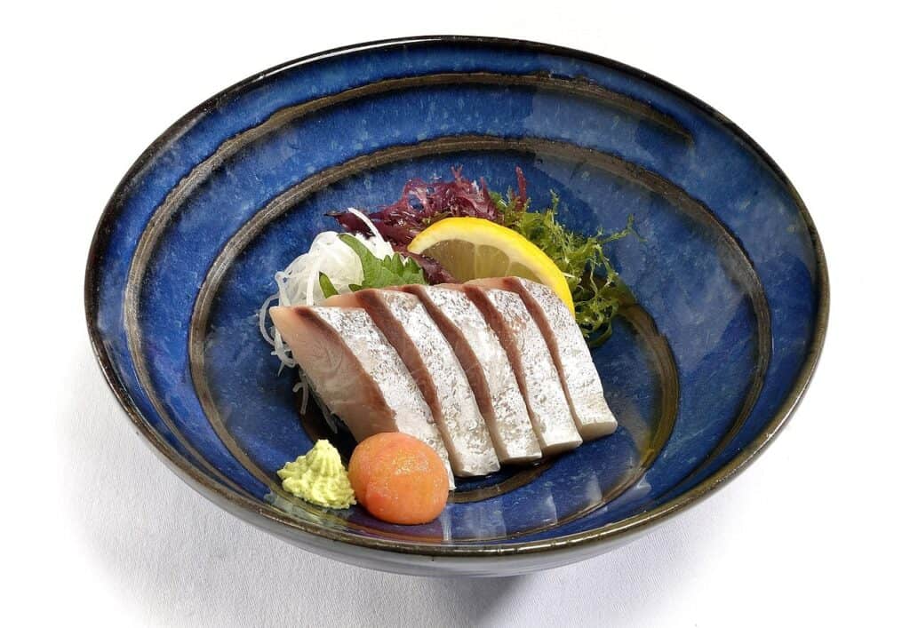 Elegantes Sashimi-Arrangement in blauer Keramikschale mit weißem Fisch, Wasabi und bunten Algen als Garnierung
