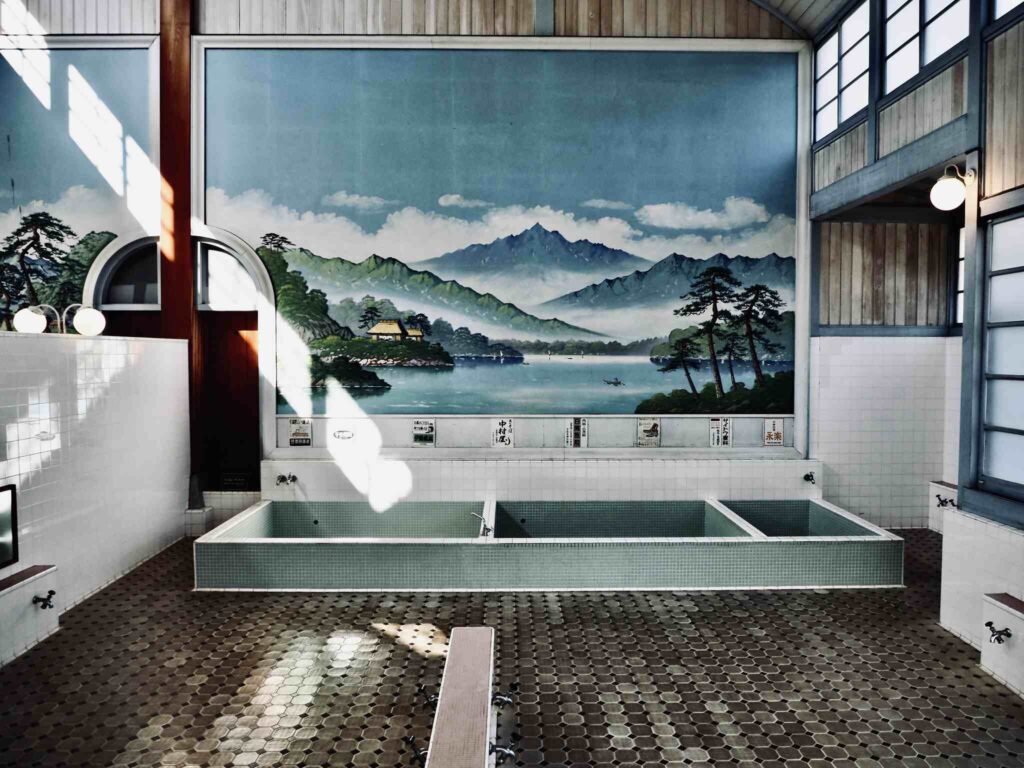 Traditionelles japanisches Onsen-Badezimmer mit rechteckigen Mineralbädern, bemalter Berglandschaft-Wandmalerei und authentischer Innenausstattung