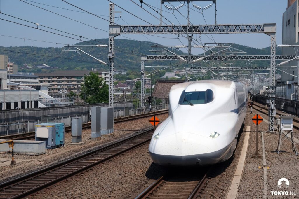 Moderner Shinkansen-Hochgeschwindigkeitszug bei der Einfahrt in den Bahnhof, mit Stromleitungen und Schienen
