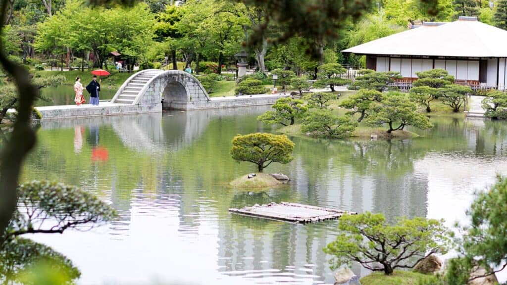 Klassischer japanischer Landschaftsgarten Shukkei-en in Hiroshima mit gewölbter Steinbrücke, Teich und Teehaus