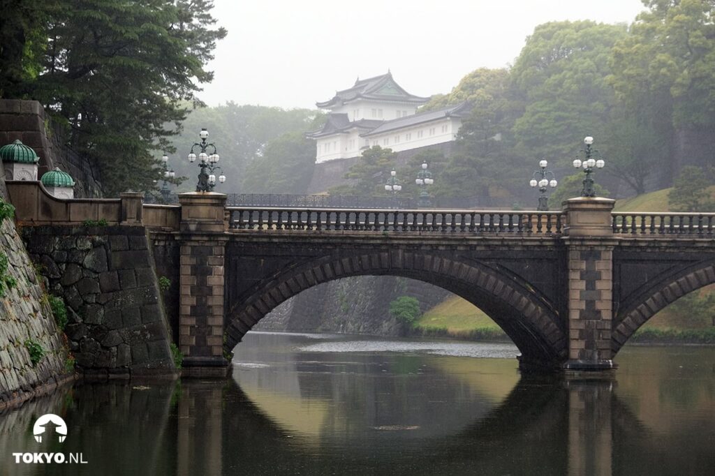 Eine traditionelle japanische Steinbrücke über einen ruhigen Wassergraben mit dem kaiserlichen Palast im Hintergrund, umgeben von üppigem Grün in Tokio.