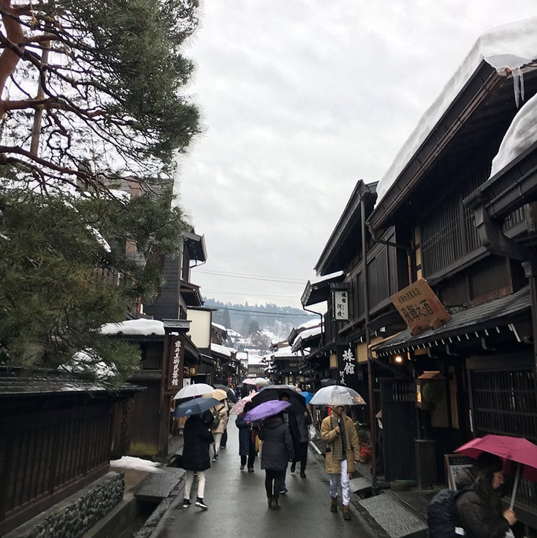 Takayama im Winter in einer Straße mit Schnee auf den Dächern und Personen in der Mitte