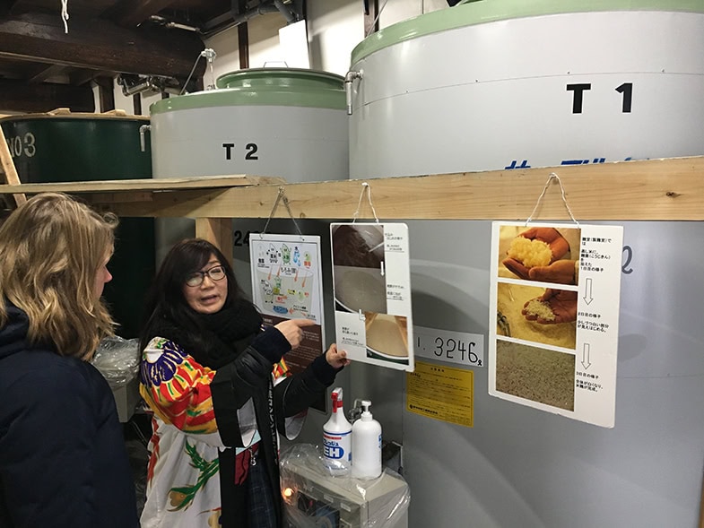 Zwei Personen im Vordergrund beim Erklären während des Sake-Brauerei Rundgangs in Takayama
