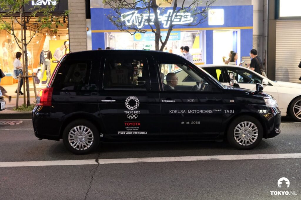 Schwarzes Taxi mit Tokyo-2020-Olympia-Branding von Toyota auf einer Einkaufsstraße in Japan