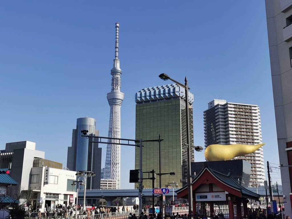 Tokyo Skytree bei klarem Himmel - Frontalansicht des Turms mit umgebenden modernen Gebäuden und dem charakteristischen gelben Asahi-Gebäude.
