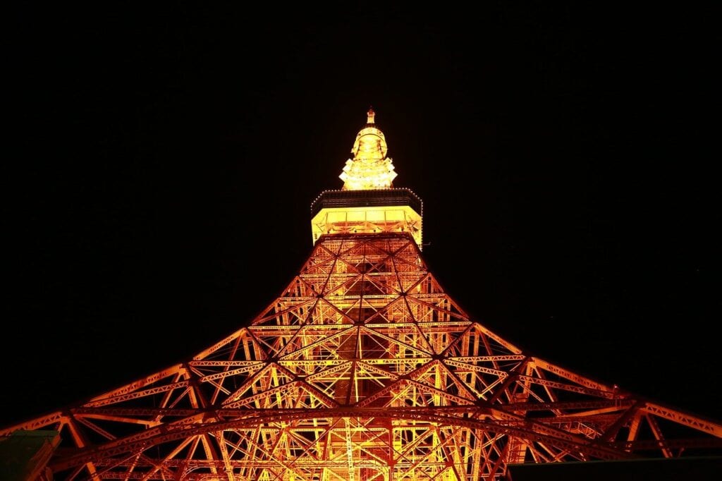 Tokyo Tower bei Nacht in leuchtend roter und gelber Beleuchtung von unten fotografiert gegen schwarzen Himmel