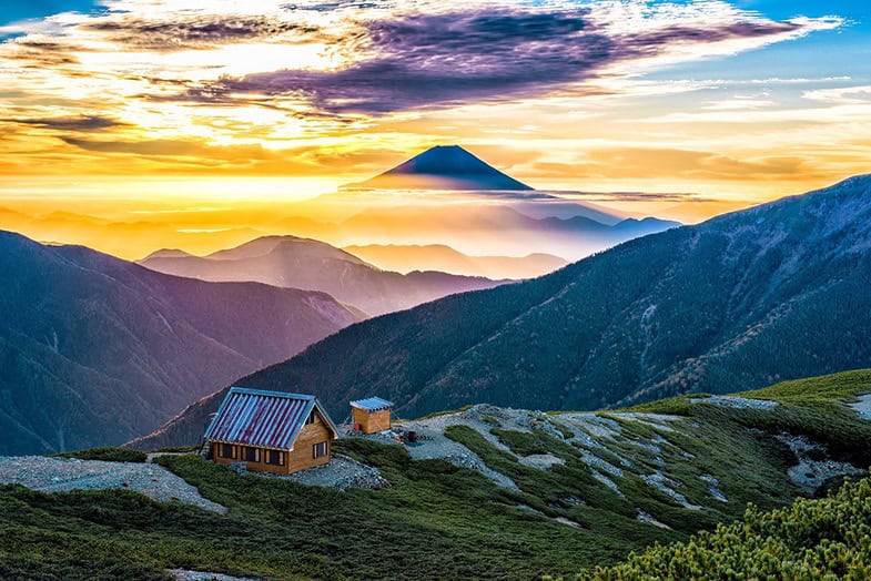 Berghütte bei Sonnenaufgang in den japanischen Alpen mit Mount Fuji in der Ferne und dramatischem Morgenhimmel