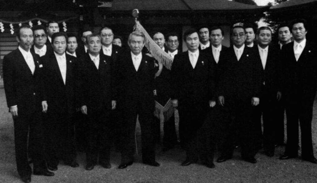 Historisches Schwarz-Weiß-Foto einer großen Gruppe japanischer Männer in formeller Kleidung (Anzüge mit weißen Krawatten), die für ein Gruppenfoto posieren.