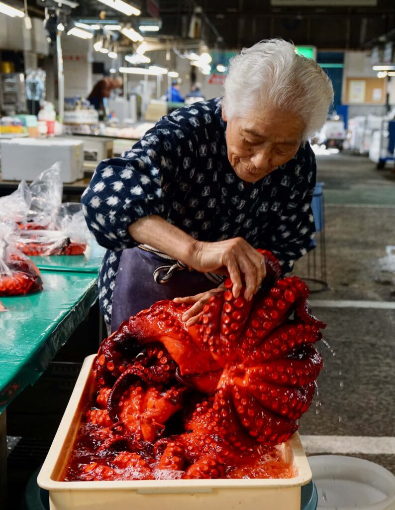 Ältere japanische Marktfrau verkauft frischen roten Oktopus am Sendaishi Chuooroshiuri Fischmarkt in Sendai