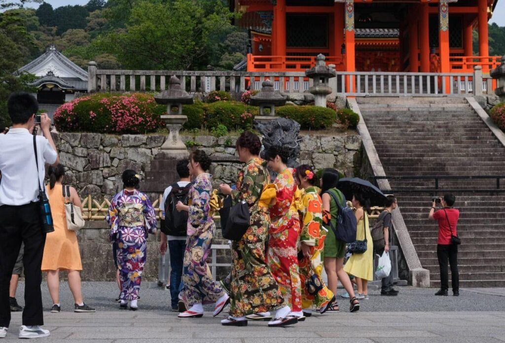 Frauen in bunten Kimonos besuchen einen roten japanischen Tempel mit Steinlaternen