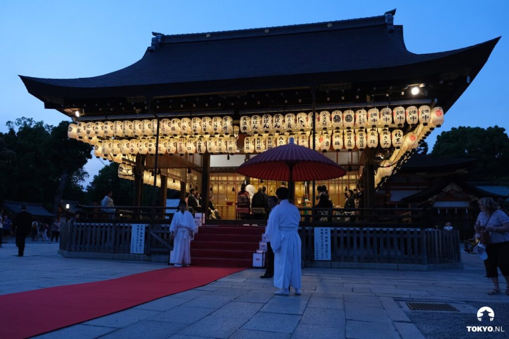 Traditioneller japanischer Schrein in Kyoto bei Abenddämmerung mit leuchtenden Papierlaternen, Miko-Priesterinnen und spiritueller Zeremonie