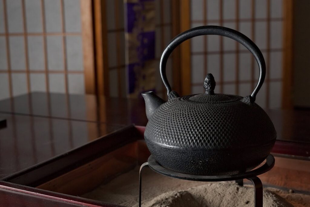 Schwarze gusseiserne Tetsubin-Teekanne mit traditionellem Muster steht auf einem Holzuntersetzer in einem japanischen Teeraum mit Shoji-Wänden
