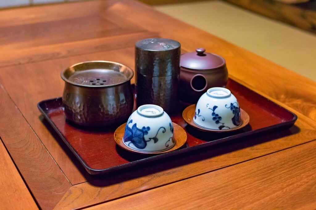 Komplettes japanisches Teeservice auf rotem Holztablett mit Teekanne, Sieb und blau-weißen Porzellan-Teeschalen mit floralen Motiven