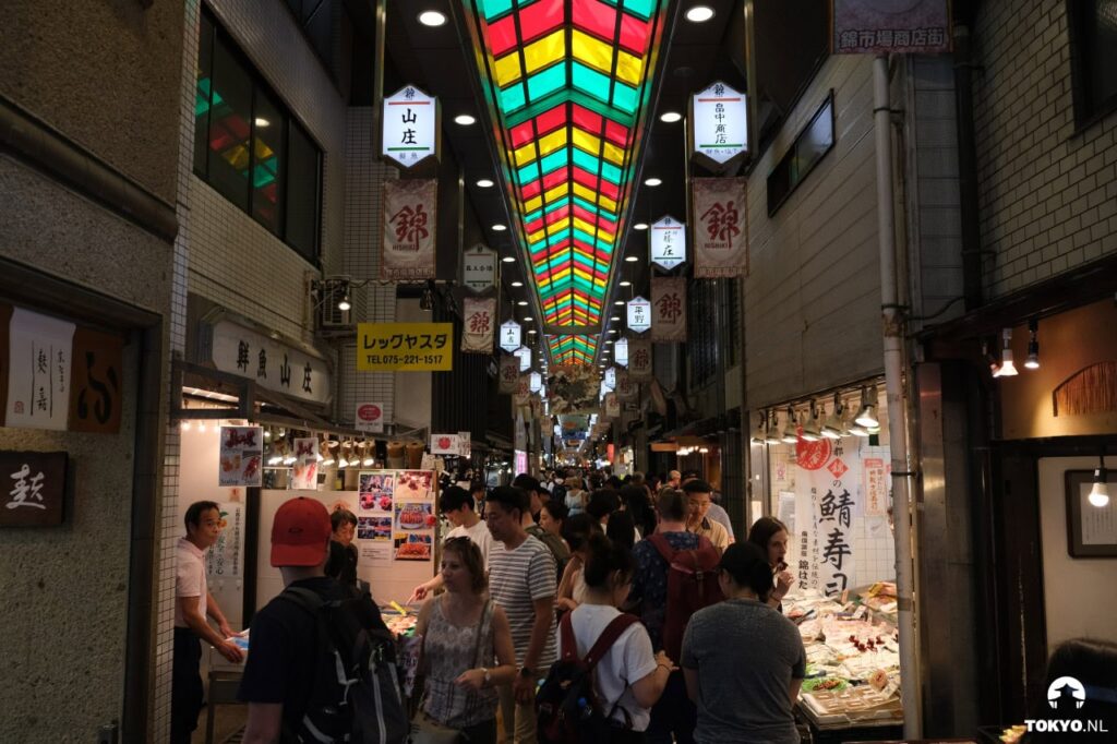 Lebendiger Nishiki-Markt in Kyoto mit bunter Glasdecke, lokalen Lebensmitteln, Sushi-Ständen und geschäftigen Besuchern beim Einkaufen