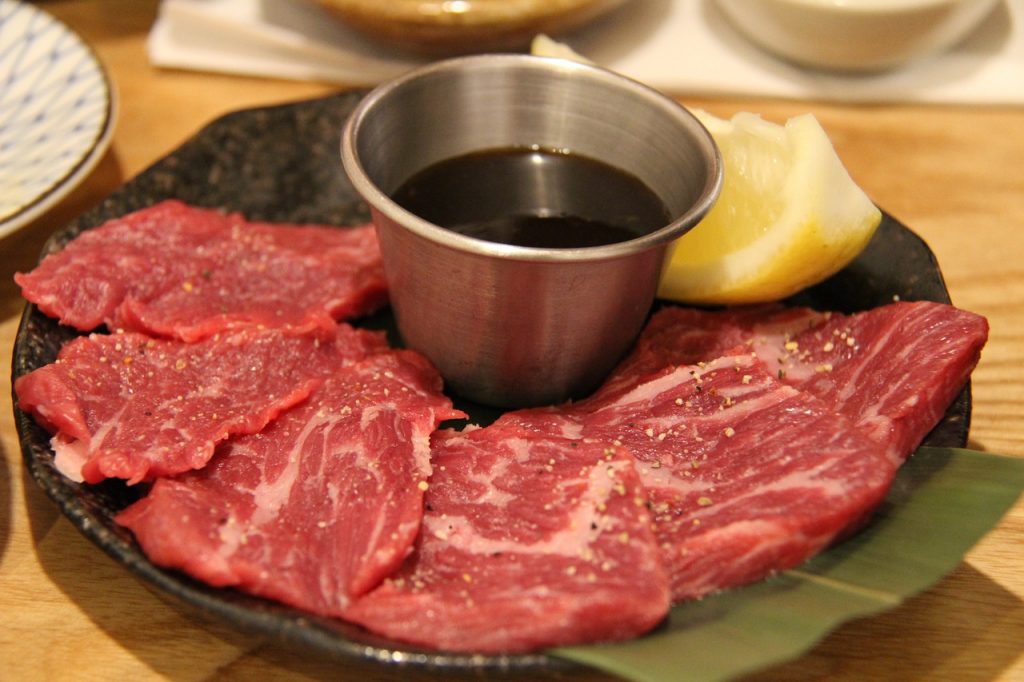 Rohe Wagyu-Fleischstücke auf schwarzem Teller mit Sojasauce und Zitrone, servierfertig für Sashimi-Style