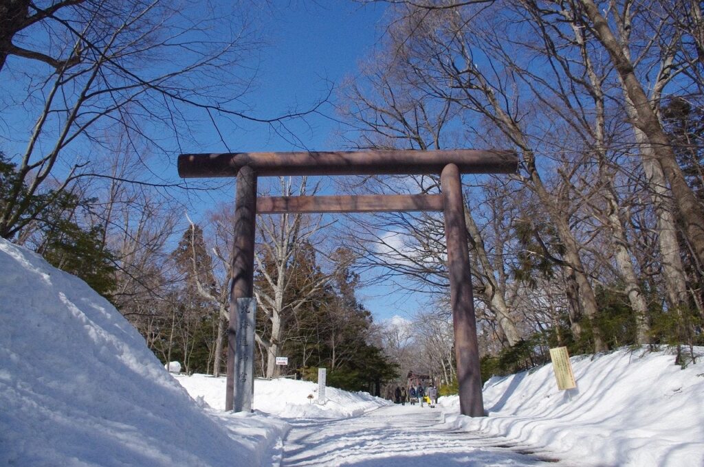 Traditionelles japanisches Torii-Tor im Schnee mit Besuchern im Hintergrund